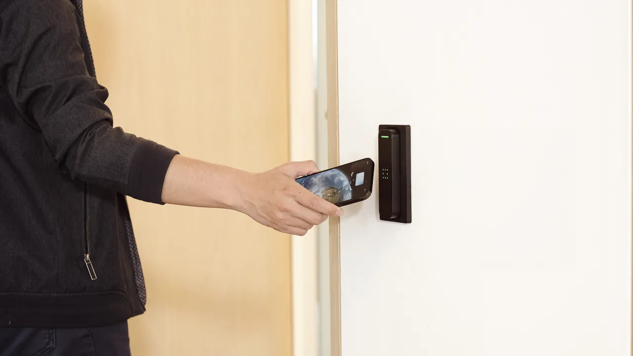 Person holding a smartphone near a Verkada access control card reader on a white door.
