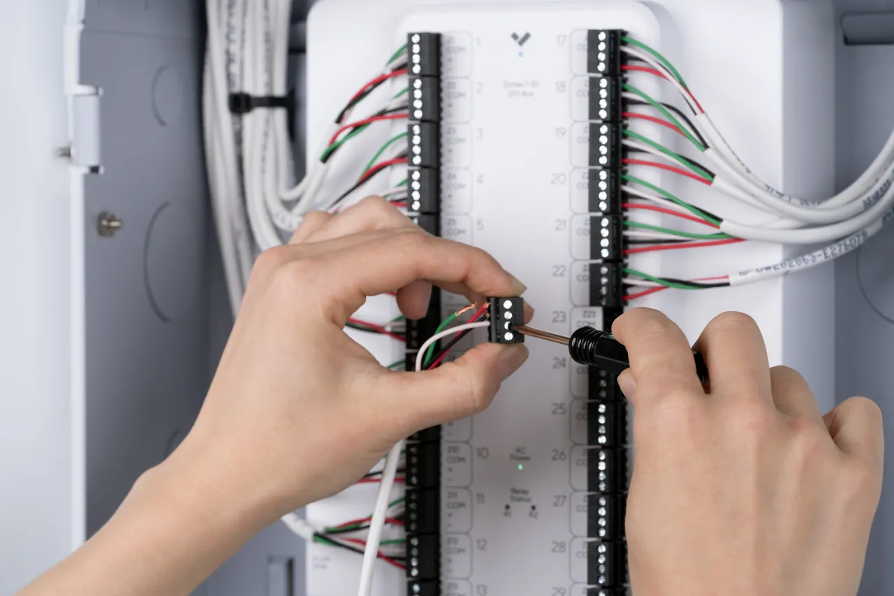 Hands using a screwdriver to connect wiring to a Verkada alarm panel.