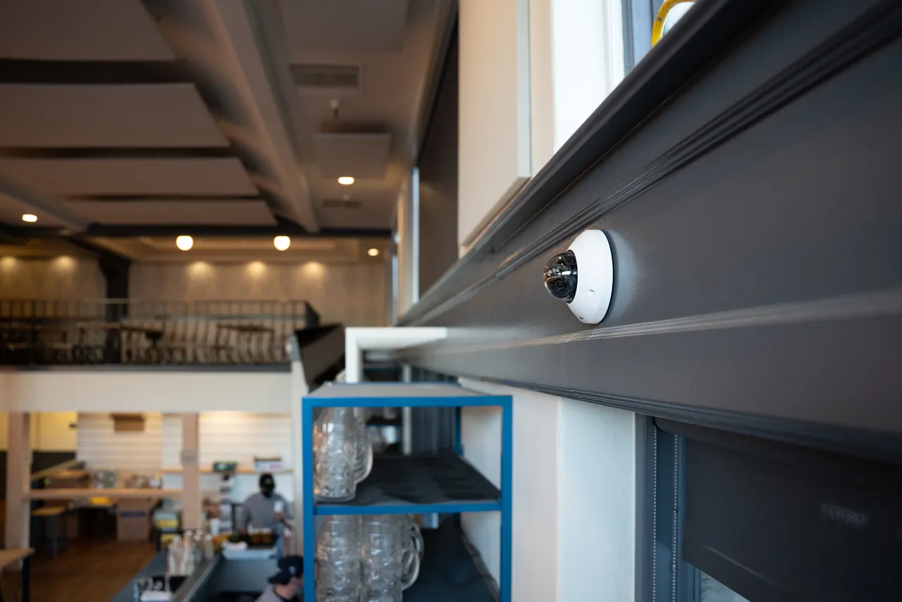 Verkada mini dome camera mounted on a gray beam inside a restaurant.