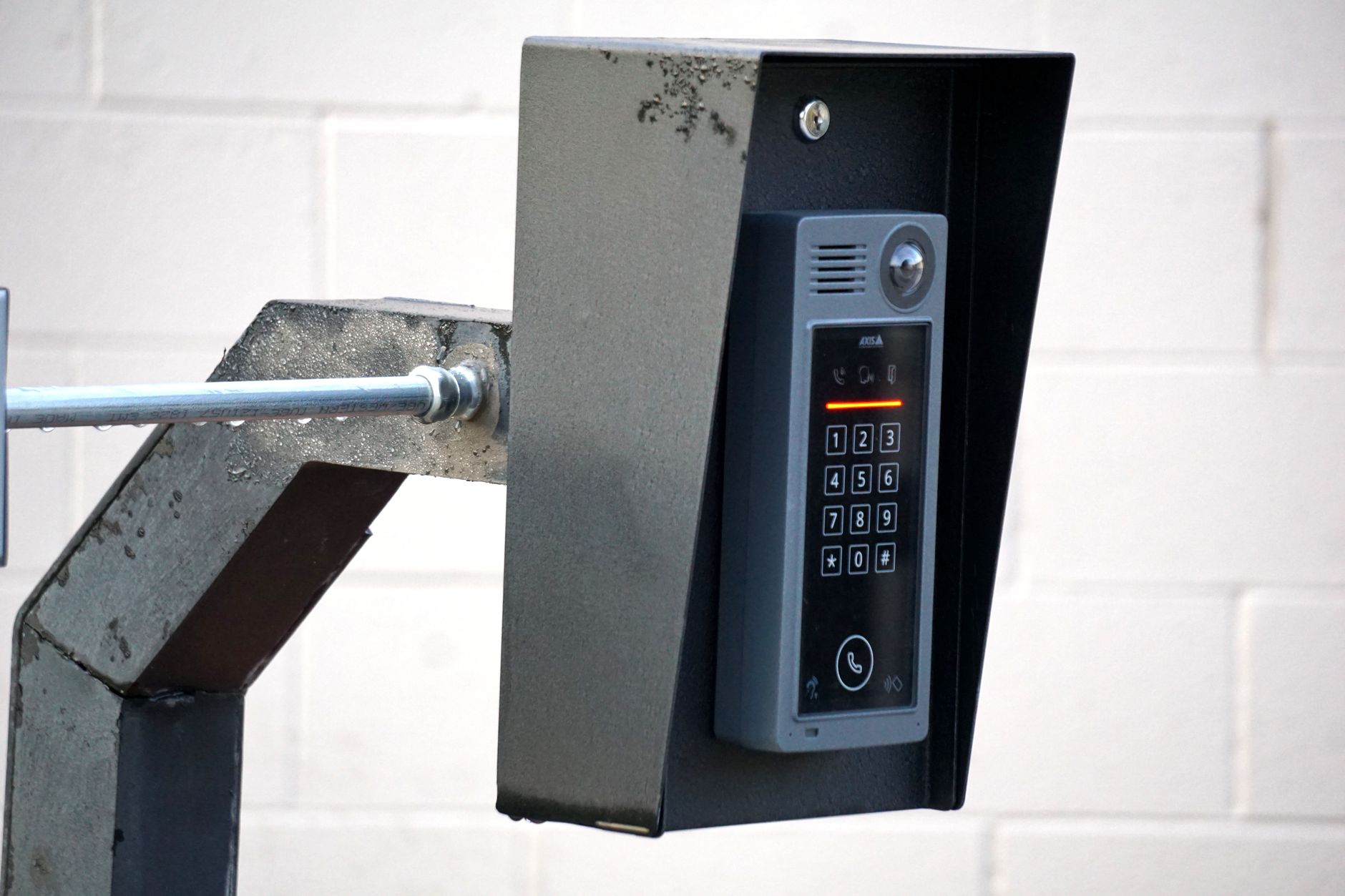 Outdoor building intercom system with numeric keypad, wide-angle camera, and call button mounted on a metal post bracket.