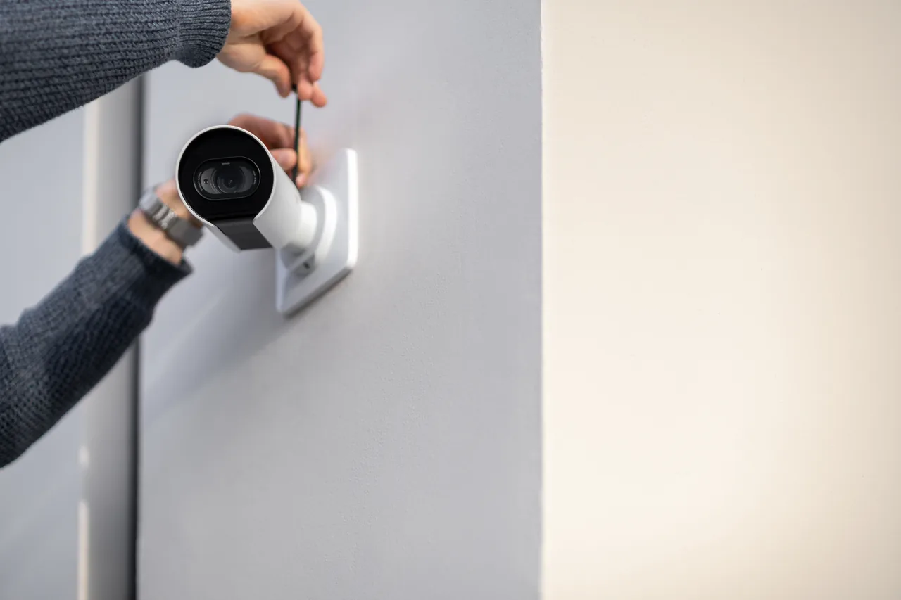 Technician using a screwdriver to mount white bullet surveillance cameras on a smooth gray interior wall.