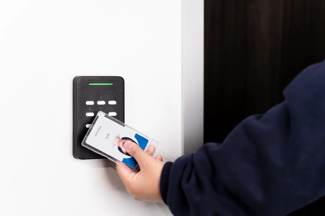 Person tapping an employee ID badge on a wall-mounted keypad reader, demonstrating a keyless entry system for business.