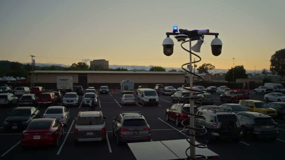 Camera mast of a mobile surveillance trailer with a strobe beacon, monitoring a lot at dusk