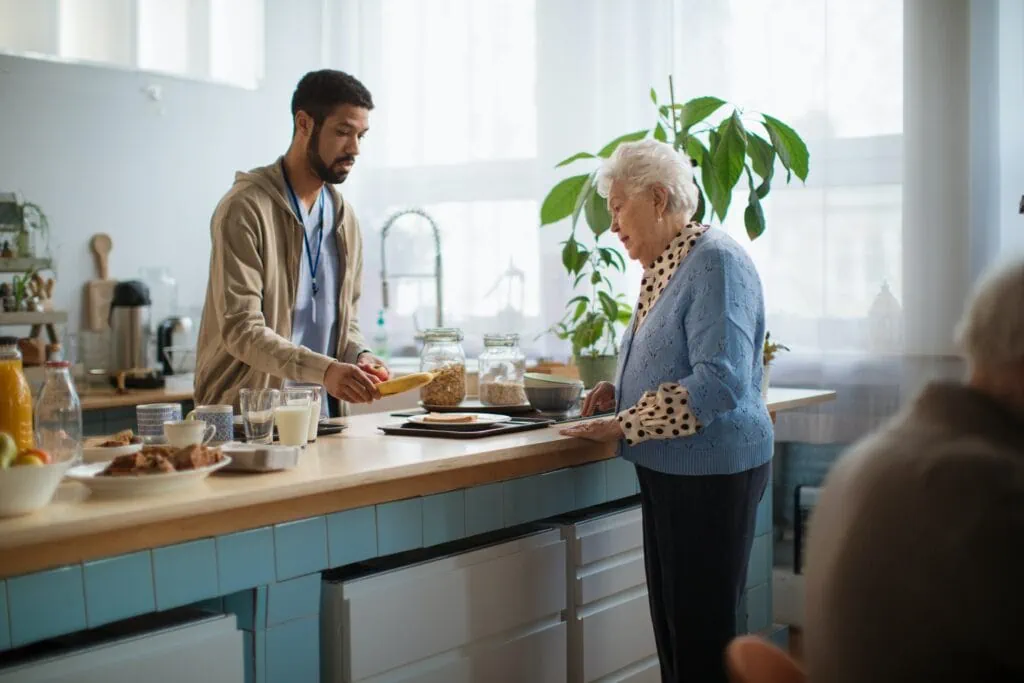 Man serving food to elderly woman in an assisted living facility that allows cameras
