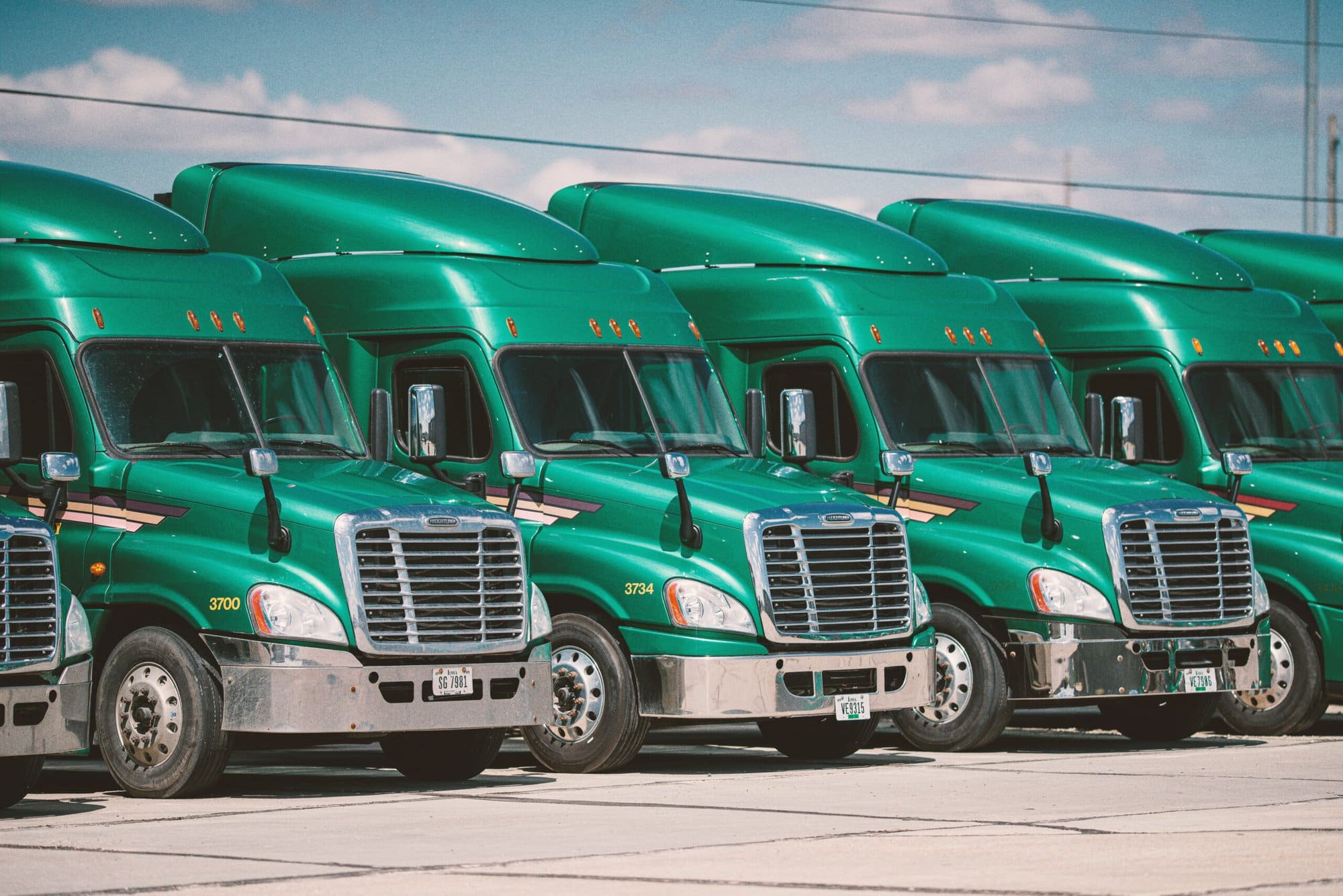 A row of green semi trucks parked in a parking lot equipped with GPS tracker dash cams.