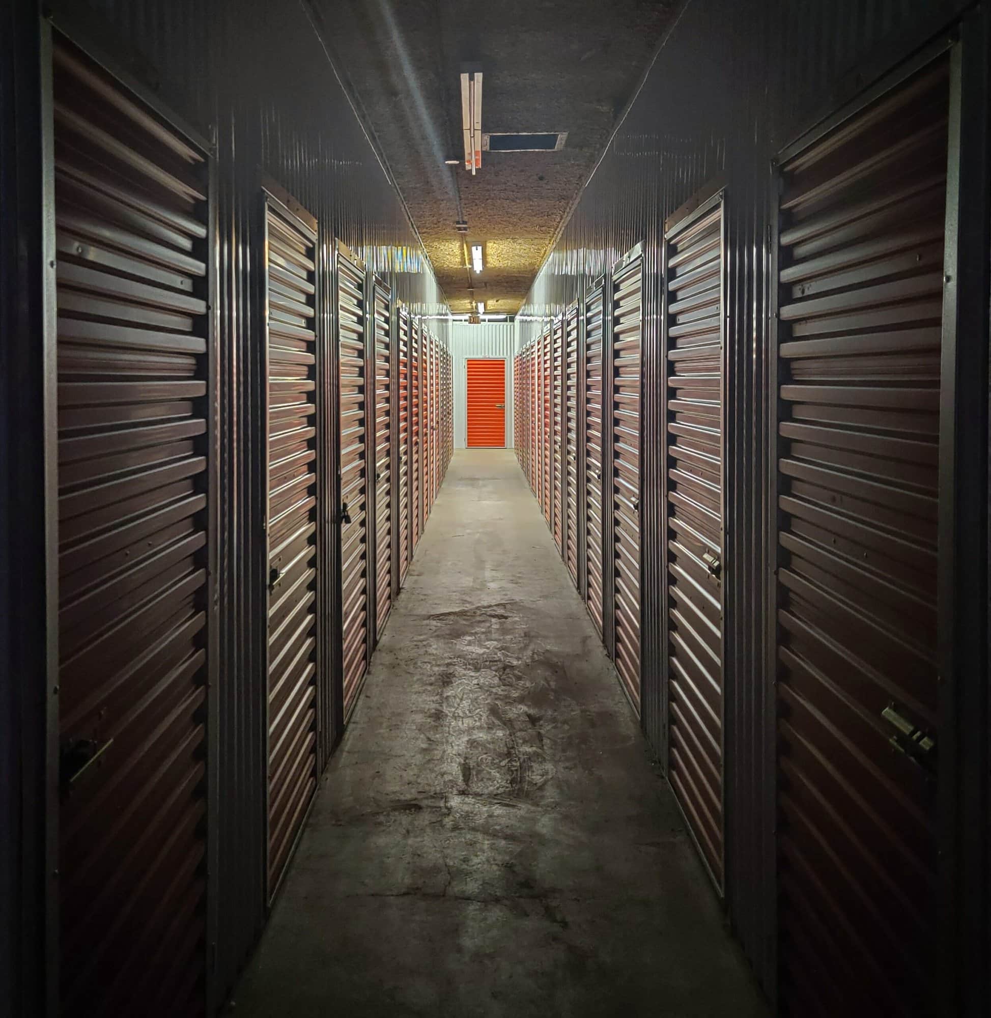 Self storage units in a hallway with a red door equipped with security cameras.